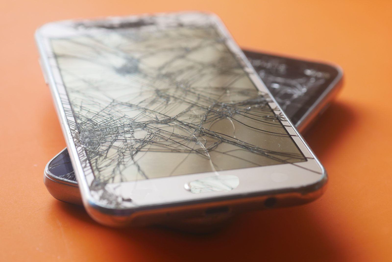 Two smartphones with heavily cracked and shattered screens on an orange background