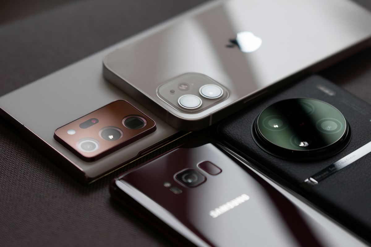Several premium smartphones from different brands stacked together on a dark surface, showing their camera modules
