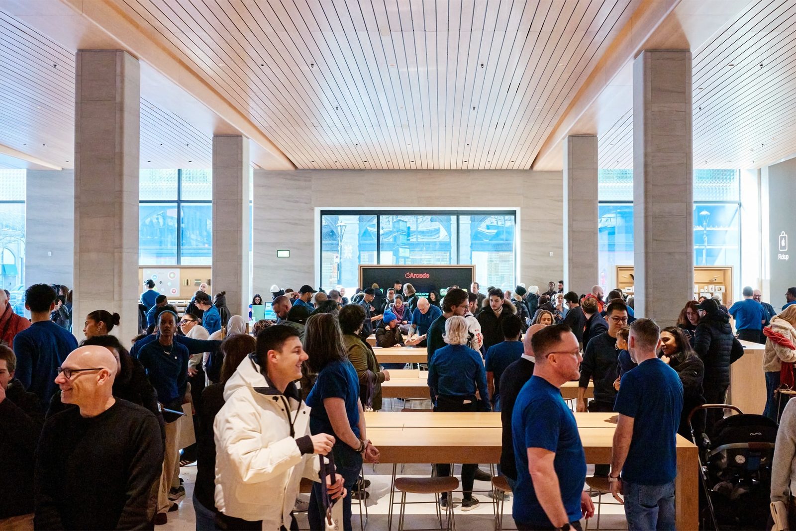 A busy Apple retail store crowded with customers and staff around wooden display tables