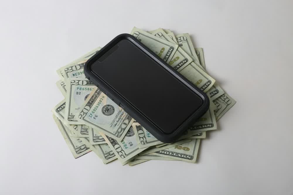 Smartphone resting on a fan of twenty dollar bills