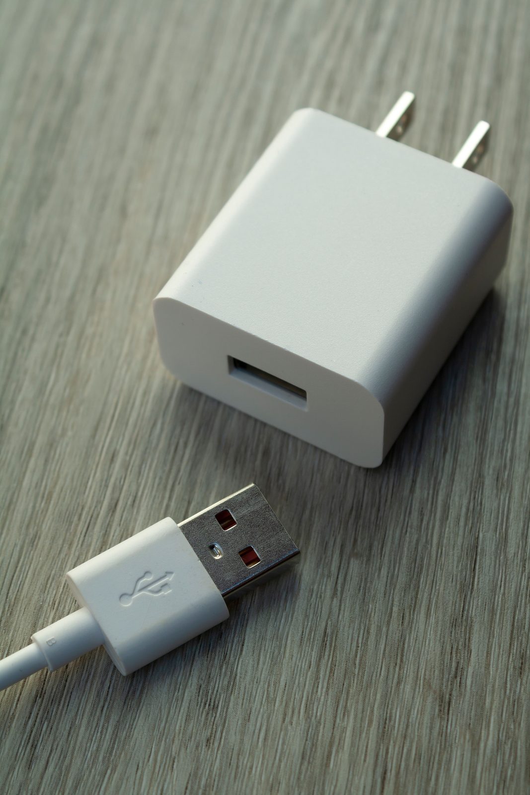 A white USB wall charger and matching cable resting on a wooden surface