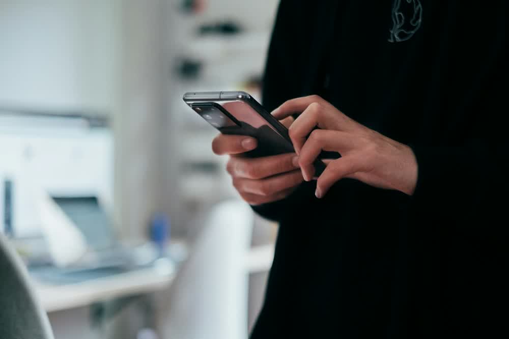Person holding a smartphone in both hands while standing at a desk