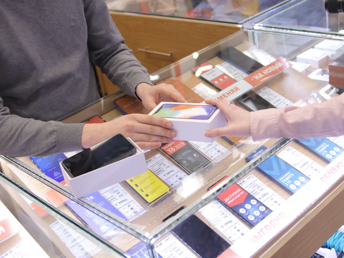 Customer handing a new phone in its box to a staff member across a phone store trade-in counter