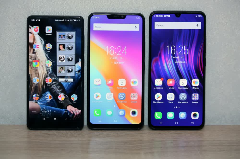 Three smartphones standing side by side on a desk with their screens on